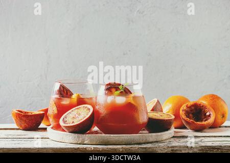 Blood orange iced cocktails in glasses, decorated by slice of oranges and fresh mint, served in ceramic tray on white wooden table with grey wall at background. Stock Photo