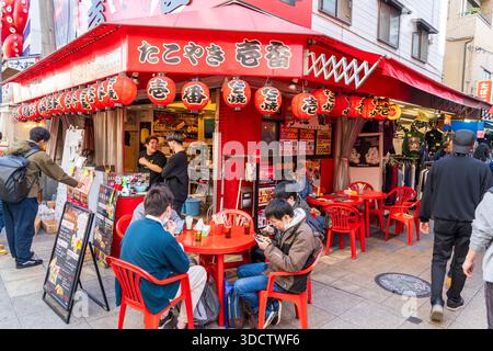 Corner Takoyaki Ichiban Osaka Sinsekaiten restaurant, Shinsekai. Large billboard with red octopus above entrance, people sitting at table with drinks. Stock Photo