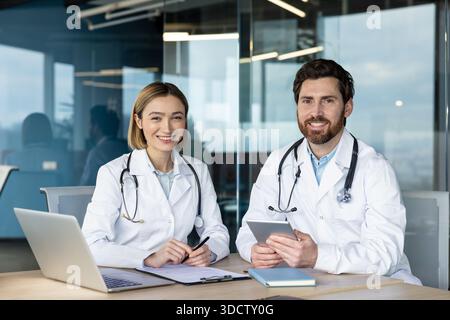 Two doctors, a woman and a man, smiling at the camera while working together in a modern clinic office, representing teamwork and healthcare professionals Stock Photo