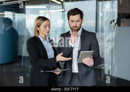 Business colleagues collaborating and discussing new strategies, solutions, and ideas while using a digital tablet and clipboard in a bright, modern corporate office environment Stock Photo