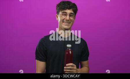 Man young hispanic holding a bottle with hand and cheeks puffed in purple studio wearing glasses and black shirt; playful curiosity. Stock Photo