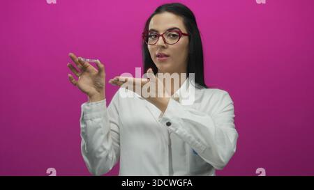 Hispanic woman dentist holding invisible braces in a pink background displaying a confident expression in a professional dental uniform. Stock Photo