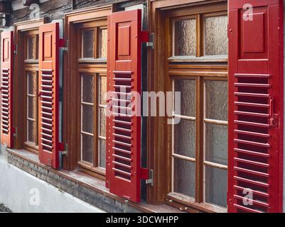 Red wooden shutters on an old building with numerous windows. Stock Photo