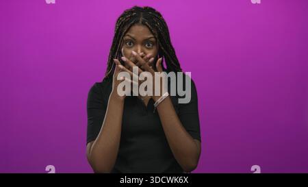 Young woman with long braided hair and hands covering mouth in magenta studio closeup; surprise wonder. Stock Photo