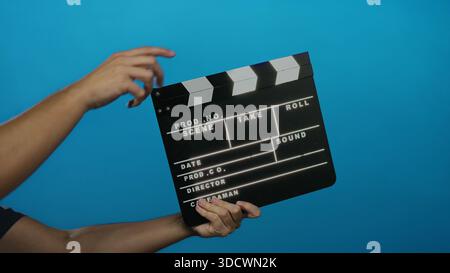 Male hand holding clapperboard against blue background ready for action in film production scene. Stock Photo