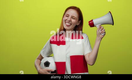 Woman holding soccer ball and megaphone in front of yellow background with red scarf, showcasing enthusiasm and energy. Stock Photo