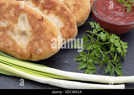 Fried patties served with tomato sauce, fresh herbs and green onion on a black slate plate, isolated on white background. Stock Photo