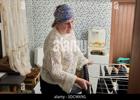 Middle aged woman hanging washed laundry on drying rack in bathroom. Stock Photo