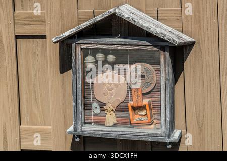 A small wooden display case with bells, a round coin motif and other lucky charms hangs on a wooden façade in Yuasa, Wakayama Prefecture, Japan. Wall shrines like this one, featuring Ebisu and Daikoku symbolism, are common on Japanese shopfronts and are meant to bring good fortune in business. Stock Photo