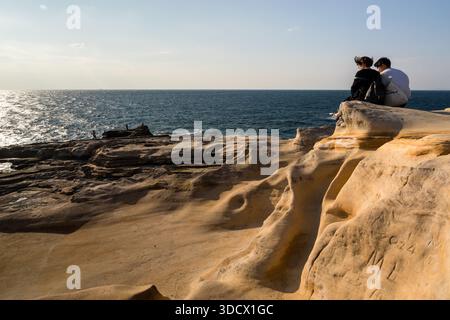 Two people sit on the rock steps of the Senjojiki plateau near Shirahama, their backpacks beside them. The sandstone terrace, uplifted from the seabed more than 15 million years ago, has been protected since 1926. Wakayama Prefecture, Japan. Stock Photo
