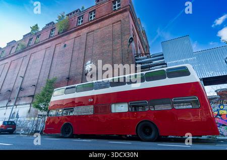 Wide-angle photograph of a red vintage double-decker bus parked in front of an abandoned industrial brick building in Berlin, Germany. Stock Photo