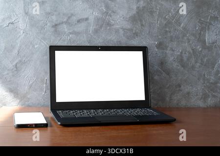 Minimal office desk scene with laptop and smartphone showing blank white screens. Ideal mockup for website, app, UI presentation, digital marketing, t Stock Photo