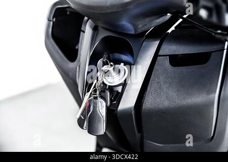 Close up of motorcycle ignition with inserted key and keychain on black body panel isolated on white background showing transport security control det Stock Photo