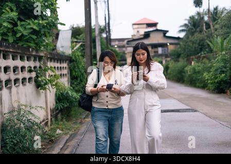 Two asian women concentrating on their mobile phones while walking on a street Stock Photo