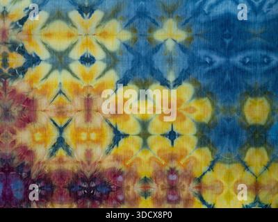 Hand-dyed cotton fabric with a repeating pattern of abstract flowers in yellow and pink against a blue background. Stock Photo