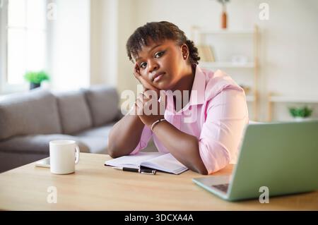 Portrait of African American woman writer sitting at working desk, looking at camera and thinking Stock Photo