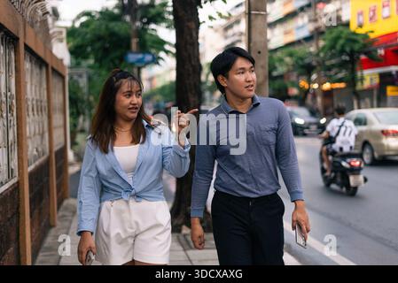 Young asian couple walking in city, woman pointing direction for man exploring urban street Stock Photo