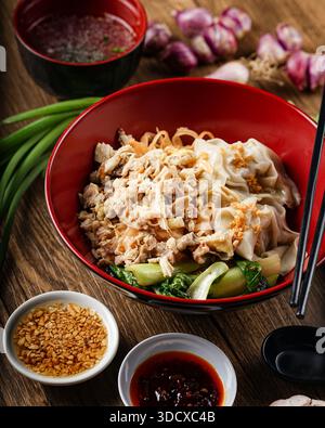 Savor the flavors of a traditional Asian noodle bowl, complete with savory meat, fresh vegetables, and a selection of condiments on a rustic wooden ta Stock Photo