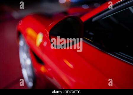 Modern red sports car exterior detail focusing on side mirror and smooth body lines with reflective paint finish and night time lighting Stock Photo