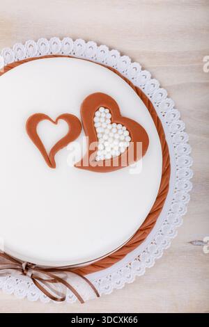 Overhead studio shot of a cake decorated with heart shapes, perfect for Valentines Day or an anniversary, set against a light wood backdrop. Stock Photo