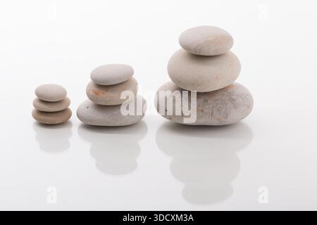 Three stacks of smooth zen stones of varying heights balanced on a white background. Suitable for meditation, relaxation, balance, and wellness concep Stock Photo