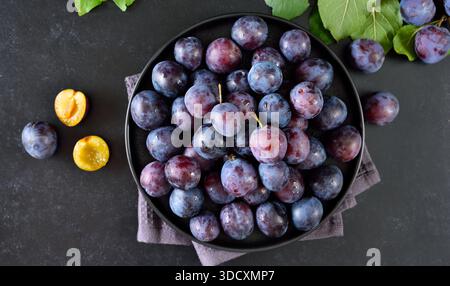 Fresh plums on plate over black stone background Stock Photo