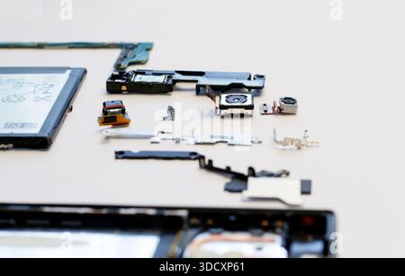 Internal components of a disassembled smartphone, including the camera module, battery, and motherboard parts, laid out on a white surface. Concept of Stock Photo