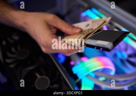 Hidden cash stored in computer memory modules, Covert operation involving cash hideaway inside memory hardware amid colorful RGB illumination and Stock Photo