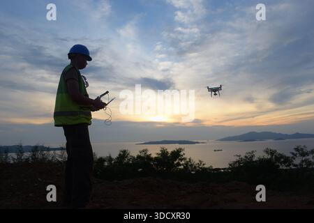 Field engineer flying a drone surveying the landscape. Sunset silhouette on top of a hill on a island. Stock Photo