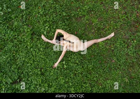 Woman practicing upavistha konasana outdoors on a green meadow, aerial view showing advanced seated yoga pose with focus on flexibility, balance and m Stock Photo