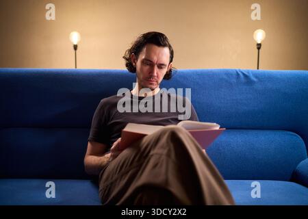 Man reads relaxingly, Relaxed man flipping through book, Individual leisurely reads on comfortable sofa, Person enjoying quiet evening with book and Stock Photo
