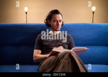 Man reads relaxingly, Relaxed man flipping through book, Individual leisurely reads on comfortable sofa, Person enjoying quiet evening with book and Stock Photo