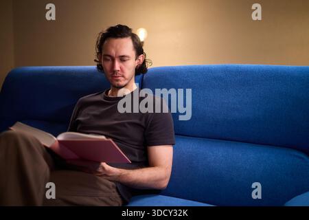 Man reads relaxingly, Relaxed man flipping through book, Individual leisurely reads on comfortable sofa, Person enjoying quiet evening with book and Stock Photo