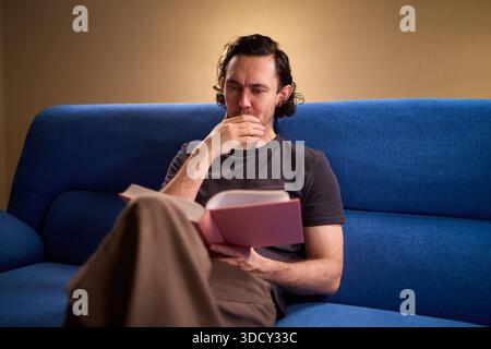 Man reads relaxingly, Relaxed man flipping through book, Individual leisurely reads on comfortable sofa, Person enjoying quiet evening with book and Stock Photo