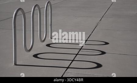 curved or wavy shadow lines on the pavement of a bicycle rack or curved installation on the sidewalk outdoors curved shadow lines horizontal backdrop Stock Photo