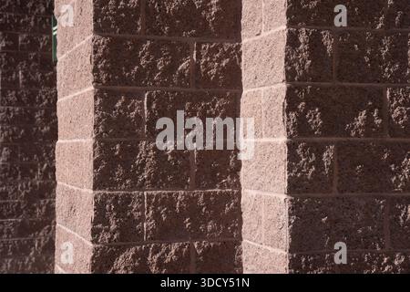 rose and pink colored stone block wall in shadow and light creating light colored stripes on exterior building wall horizontal backdrop background or Stock Photo