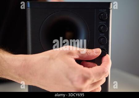 Adjusting bass knob in listening space, Technician modifies subwoofer settings in cozy setup, Close examination of audio equipment controls under warm Stock Photo