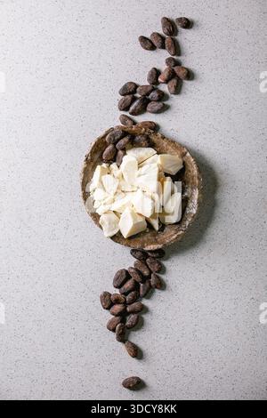 Chopped pieces of raw organic cocoa butter in craft ceramic plate and cocoa beans over grey spotted background. Flat lay, copy space Stock Photo