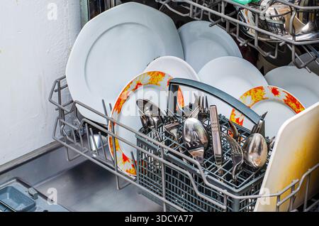 A close-up view of a dishwasher rack filled with clean white plates and silverware, showcasing a domestic chore Stock Photo