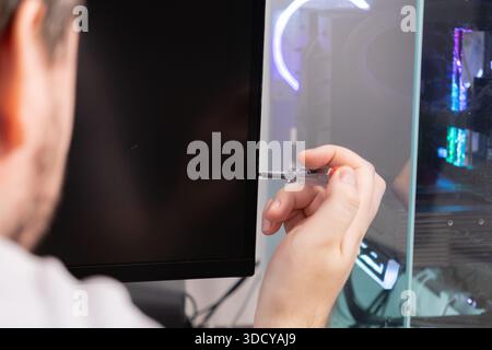 Close-up view of a professional's hand holding a clear voltage tester, meticulously inspecting the side of a modern computer monitor for electrical is Stock Photo