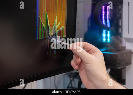 Close-up of a hand with tweezers extracting a glass piece from a cracked monitor screen, revealing pixel lines, emphasizing hardware failure and repai Stock Photo