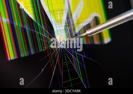 A detailed shot of a severely shattered digital screen displaying vivid dead pixels and intricate cracks, a precision tool implying urgent electronic Stock Photo