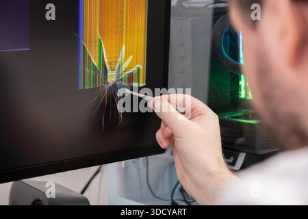Close-up view of a professional technician meticulously removing a small piece of glass from a severely damaged monitor screen displaying colorful bro Stock Photo