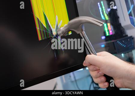 Close-up view of a human hand holding a heavy metal hammer shattering a black computer monitor, showing colorful broken pixels and symbolizing digital Stock Photo