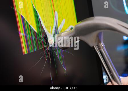 Close-up of a metal hammer hitting a black computer screen, creating widespread cracks and colorful pixel artifacts, useful for themes of frustration, Stock Photo