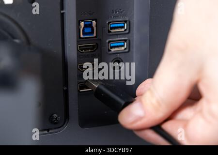 Close-up of a human hand connecting a black video cable into the HDMI IN 1 port on the back of a desktop monitor, symbolizing tech setup and connectiv Stock Photo