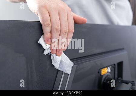 Hand carefully removes dust from a modern monitor's rear casing with a disposable cleaning cloth, representing thorough equipment sanitation and a cle Stock Photo