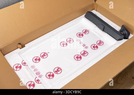 Top view of an open delivery box revealing components of a new electronic monitor, packed with protective foam and plastic film featuring child safety Stock Photo