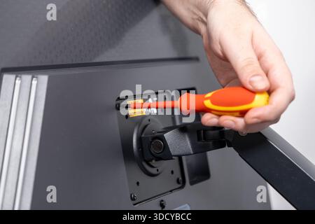 Close-up of a person's hand skillfully using an insulated screwdriver to attach a monitor to a desk mount, highlighting precise technical assembly and Stock Photo