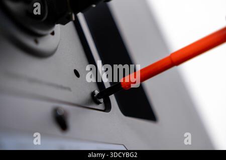 Focus on orange screwdriver turning silver screw on dark equipment, illustrating precise work for assembly, repair, or general technical maintenance n Stock Photo